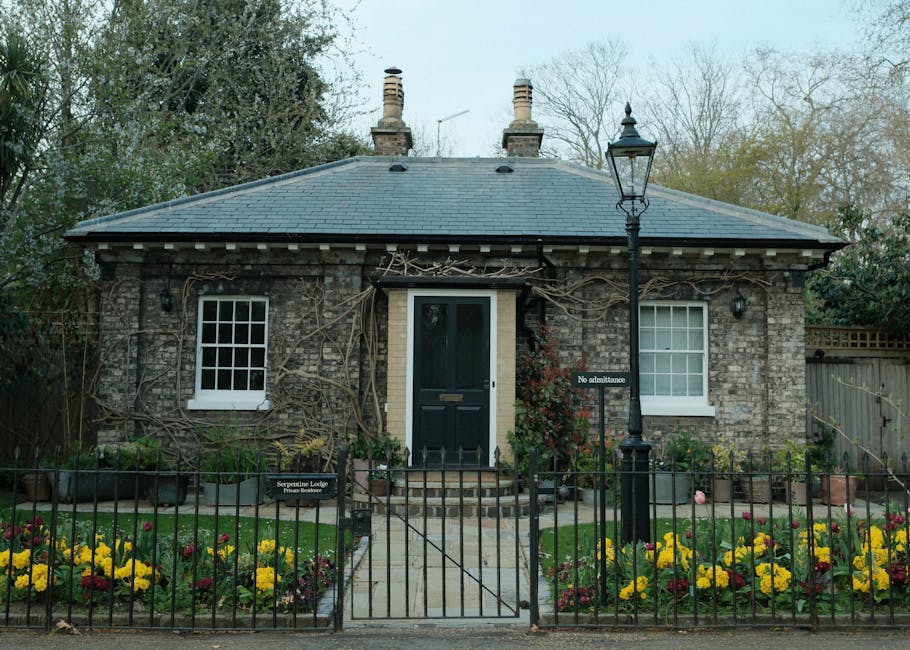 A quaint garden scene featuring a small, charming wooden garden shed with a pitched tiled roof, partially obscured by lush green foliage and flowering plants. The garden is bordered by dense shrubs and hedges, with a gravel pathway winding through the vibrant vegetation. Sunlight filters through the overhanging branches, casting dappled light on the textured soil and well-maintained lawn areas. The scene displays various textures, including smooth gravel, leafy shrubs, and the tiled roof, with tools such as pruning shears or garden rakes visible nearby, indicating ongoing garden maintenance by Gardeners Swiss Cottage. The layout suggests careful landscaping, with defined garden beds and a peaceful outdoor environment perfect for outdoor care or garden upkeep activities, aligning with the theme of the Swiss Cottage gardeners guide to Adelaide Road gardens.